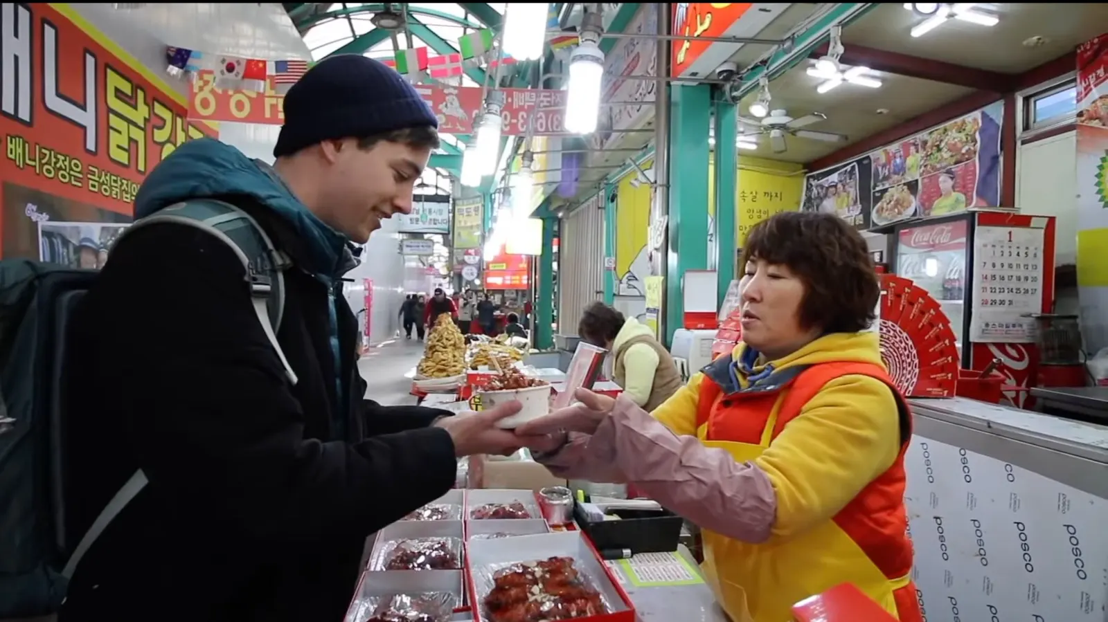 A Korean market vendor handing a cup of fried chicken to a customer